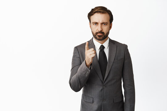Image of serious boss scolding you, businessman shaking finger, furrow eyebrows, taboo sign, standing in suit over white background