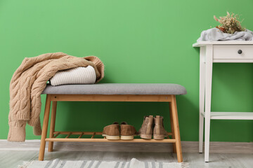 Stylish pouf with clothes and table near green wall