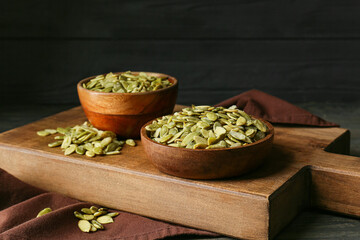 Bowls with pumpkin seeds on wooden background