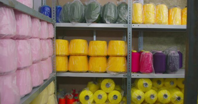 metal rack shelves with thick bobbins of bright colourful threads wrapped with polyethylene in storeroom close zoom IN and out