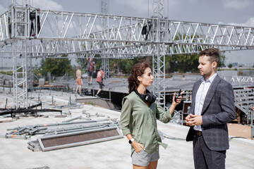 Event managers discuss stage construction. Installation of stage equipment and preparing for a live concert open air. Event manager portrait. Summer music city festival. Teamwork. - 470273065