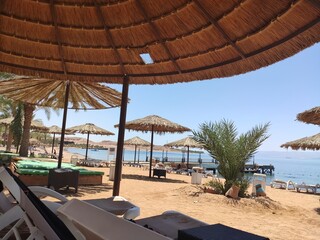 Fototapeta na wymiar Plage près de la mer Rouge en Jordanie, sur une plage exotique, avec des transats, des parasols en paille, côté Tahiti, avec de la végétation, reconfort pendant un séjour, sous une forte chaleur