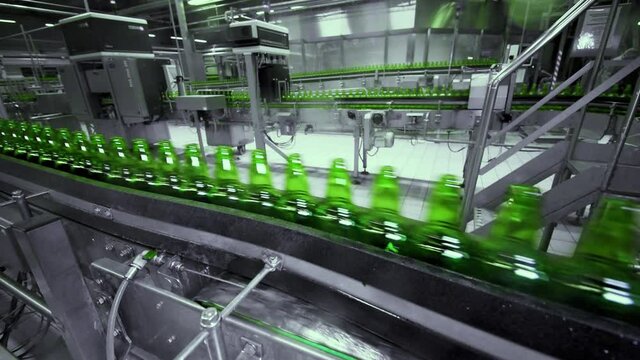 line for filling beer in a brewery. Empty green glass bottles moving on a conveyor belt in a queue at a beer factory.