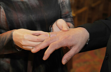 Gold ring that the bride places on the groom's finger on her wedding day. Close up view of hands.
