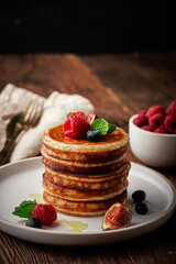 Tasty appetizing homemade pancakes served with honey, raspberries and blueberries on plate on dark background