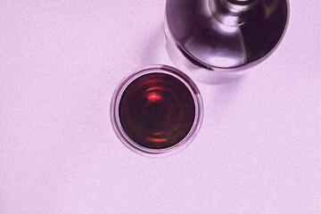 A glass of red wine and a bottle of wine on a pink background.