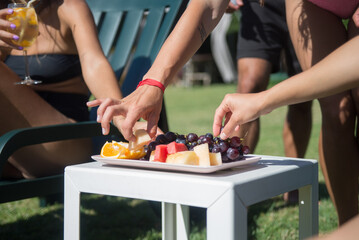 Close-up of fruit bowl near swimming pool. Melon, watermelon, orange and grapes on plate, people taking fruits. Leisure, food, party concept