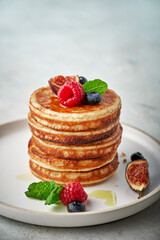Tasty appetizing homemade pancakes served with honey, raspberries and blueberries on plate on grey background