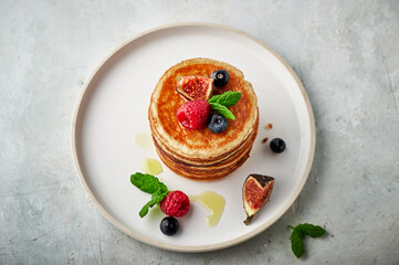 Tasty appetizing homemade pancakes served with honey, raspberries and blueberries on plate on grey background