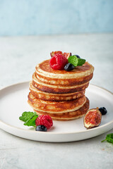 Tasty appetizing homemade pancakes served with honey, raspberries and blueberries on plate on grey background
