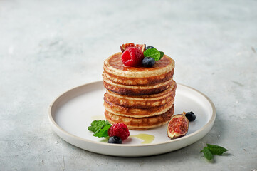 Tasty appetizing homemade pancakes served with honey, raspberries and blueberries on plate on grey background