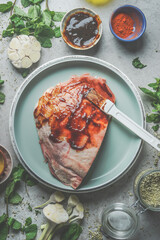 Raw meat with homemade marinade on blue plate with garlic, spices and herbs on grey concrete background. Meat preparation for BBQ or grill. Top view.