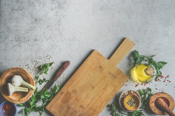 Food background with wooden cutting board, fresh herbs, garlic, olive oil, mortar and pestle, ...