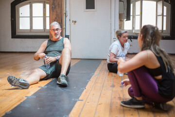 Tired senior dance group taking break. Adults resting after dance class drinking water and talking. Dance, hobby, healthy lifestyle concept