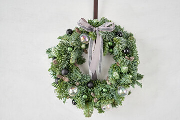 Beautiful festive wreath of fresh spruce on Gray wall. Xmas circlet with ornaments and balls....