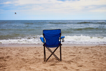 Blue folding chair back on sea beach, without people, beach holiday alone, loneliness