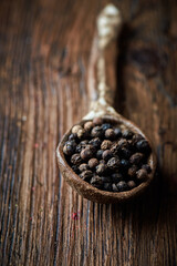Black pepper on an ceramic spoon over wooden backround
