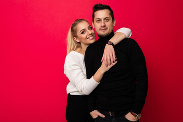 Photo of a beautiful pretty amazing positive smiling happy young blonde woman with makeup and ponytail in a stylish white knitted sweater and black pants and an adult brunet man with stubble in a