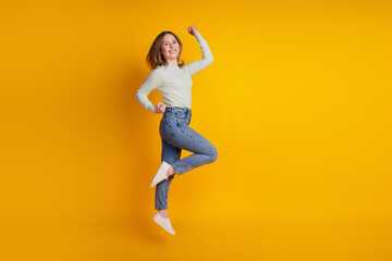 Fototapeta na wymiar Photo of astonished funky sporty lady jump rejoice win wear green shirt jeans sneakers isolated on yellow background