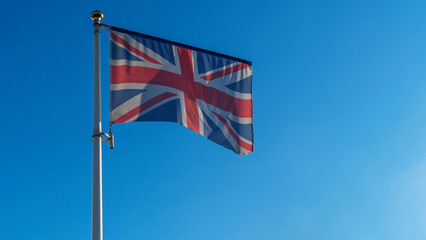 The flag of United Kingdom waving on wind on blue sky background. British union jack flag waggling in the wind.