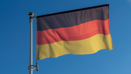 German flag with stripes in black, red, gold on a pole, is fluttering with frayed seam in the wind against a blue sky.