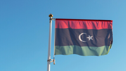 National flag of Islamic republic of Libya on a flagpole in front of blue sky with sun rays. Diplomacy concept.