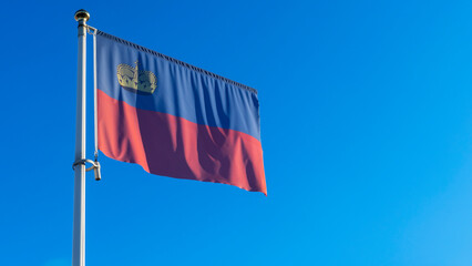 National flag of Liechtenstein on a flagpole in front of blue sky with sun rays and lens flare. Diplomacy concept.