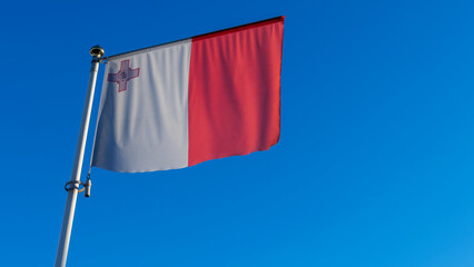 National flag Republic of Malta on a flagpole in front of blue sky with sun rays and lens flare....