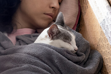 Sleeping with the female cat. A woman sleeping in a hammock with her white female cat wrapped in a blanket. Cat lover. Animal lover. Lifestyle.