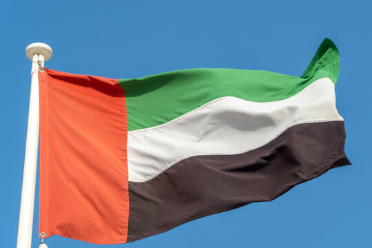 United Arab Emirates (UAE) Flag hanging and blowing in sunshine on blue sky background.