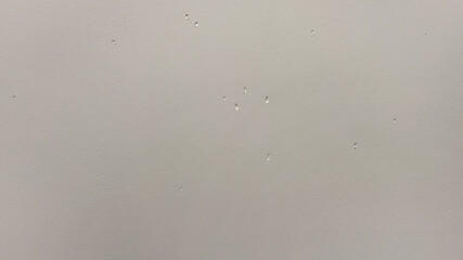 A gray smooth wall with damage and potholes. Light texture with dents.