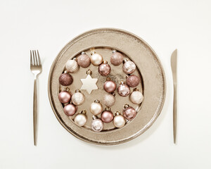 Christmas plate, festive table setting concept, sparkling small balls beige pink color and star in metal plate, knife, fork. New Year dinner or party idea with xmas decoration