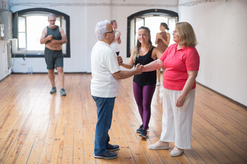 Young Caucasian dance instructor teaching senior couple. Smiling female teacher with long fair hair showing moves to elderly partners. Dance, hobby, healthy lifestyle concept