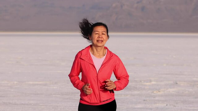 Asian woman jogging across the Bonneville Salt Flats flats in Utah.
