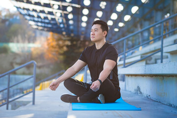 handsome asian man meditating in modern urban stadium, sitting lotus pose Male practicing yoga mat, zen. relaxes outdoors in nature in the morning Concept healthy lifestyle, relax, calm, meditation