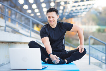 handsome asian fitness coach holds workout classes online using video call webcam and laptop....