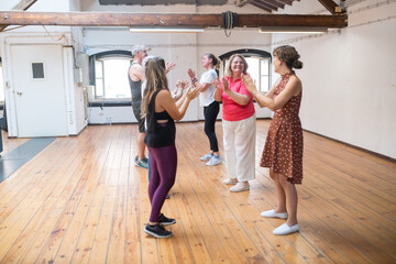 Happy retired dance students clapping their hands with teacher. Group of senior Caucasian dancers clapping hands together with young instructor in dance studio. Dance, hobby, healthy lifestyle concept