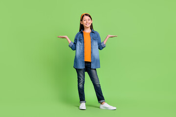 Full size photo of funny preteen girl hold hands wear shirt jeans hairband shoes isolated on green background