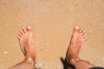 Men's bare feet stand on the sandy beach. Top view, flat lay