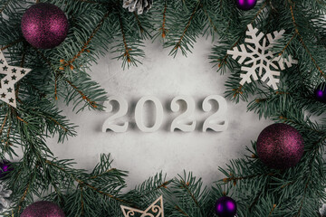 Numbers 2022 on white surface with branches of Christmas tree, decorations, purple balls. Happy New Year 2022. Top view