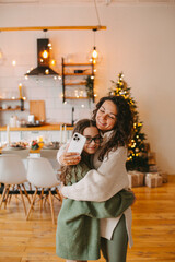 Happy young woman with cute teenage daughter in christmas interior is photographed on phone.