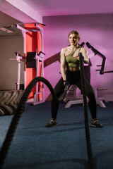 Strong fitness woman doing crossfit exercises with ropes at the gym