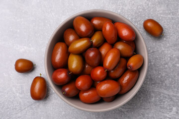 Fresh Ziziphus jujuba fruits with bowl on light table, flat lay