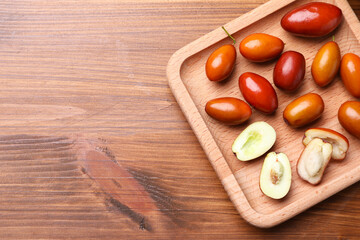 Wooden plate with fresh Ziziphus jujuba fruits on table, top view. Space for text