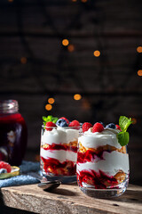 On a wooden background with lights, dessert with cream, cottage cheese, raspberries and blueberries in a glass