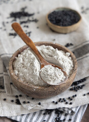 Bowl with a spoon of black lentils flour and beans on white wooden table close up