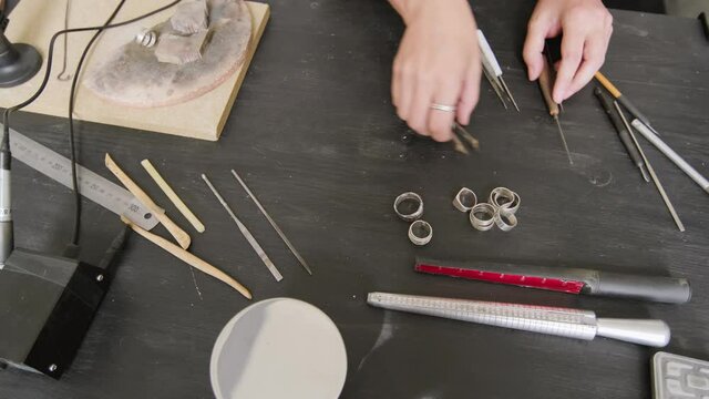 Top view tracking shot of hands of unrecognizable jeweler arranging tools on her workbench