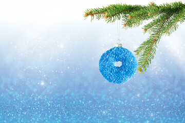 Christmas snowy decoration with hanging blue glitter donut and fir tree branch on blurred shiny...