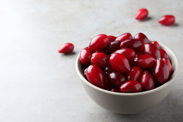 Fresh ripe dogwood berries in bowl on light grey table. Space for text