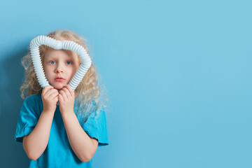 cute caucasian girl with curly blonde hair playing with pop it tube toy on blue background